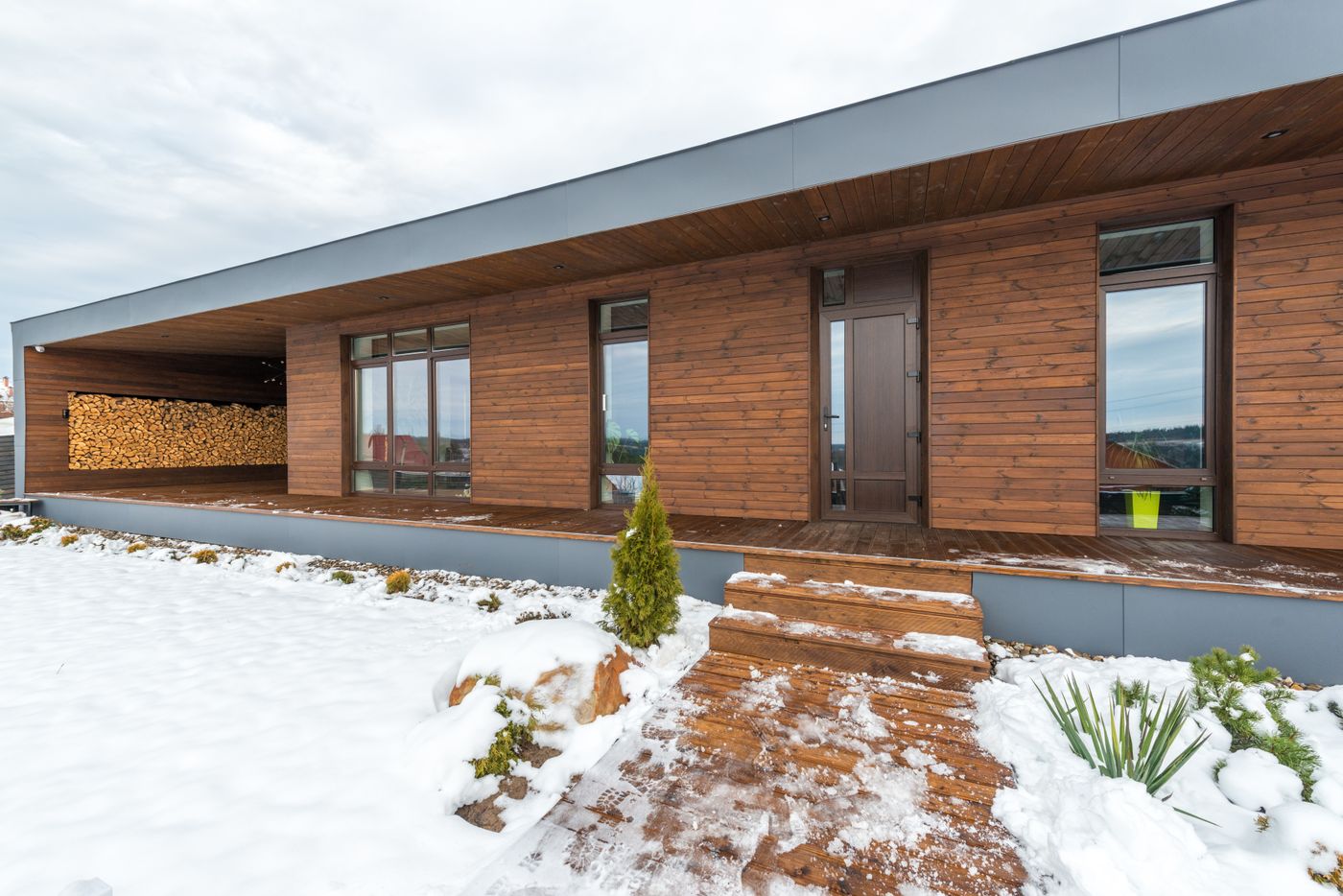Maison contemporaine en bois avec réserve de bûches sous la neige